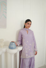 تصویر گیلری ویور میں لوڈ کریں، A woman models a lavender purple traditional outfit with white floral embroidery, standing in a bright white room next to a white pedestal holding a blue ceramic pot.