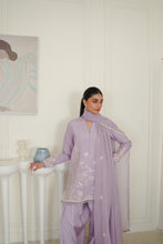 تصویر گیلری ویور میں لوڈ کریں، A woman models a lavender purple traditional three-piece outfit with matching pants and dupatta, featuring white floral embroidery and pearl trim, set against a white paneled wall background.
