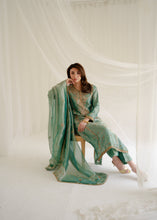 Load image into Gallery viewer, Woman in a green traditional outfit sitting on a white draped background