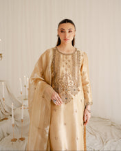Load image into Gallery viewer, Woman wearing a beige embroidered traditional outfit in a decorated room with candles.