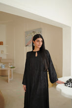 تصویر گیلری ویور میں لوڈ کریں، A woman wearing a long black embroidered shirt with a keyhole neckline and sleeves, standing in a bright, modern interior room.

