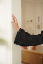 تصویر گیلری ویور میں لوڈ کریں، A person's hand resting against a white doorframe, wearing a black long-sleeve dress with decorative lace trim.
