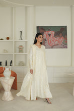 Load image into Gallery viewer, A woman models a long-sleeved, off-white embroidered traditional dress in a bright, modern white room with built-in shelves and decorative furniture.
