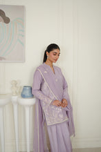 تصویر گیلری ویور میں لوڈ کریں، A woman models a lavender purple traditional three-piece salwar kameez set with white floral embroidery and bead trim, standing in a minimalist white room.
