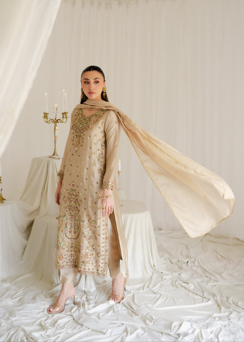 Woman in a gold embroidered outfit with a beige scarf in a white, draped setting.